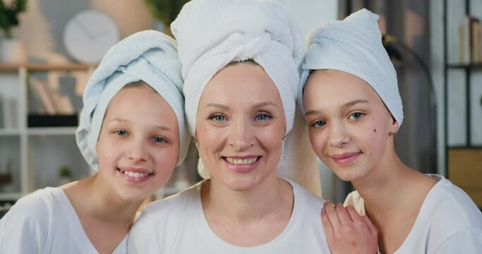 Smiling woman mother and her two teen girls daughters in terry towels posing on camera in contemporary home interior