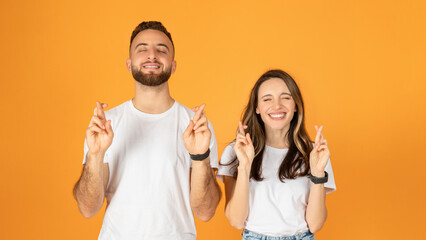 Joyful young couple with eyes closed, fingers crossed for good luck