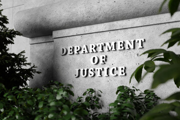 Silver sign of Department of Justice on a classical concrete wall with plants as foreground. Illustration of the concept of enforcement of federal laws