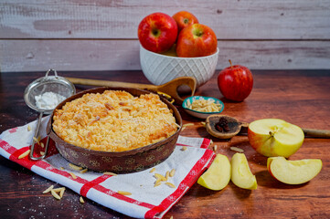Freshly baked apple pie on a rustic kitchen worktop with ingredients and kitchen utensils.
