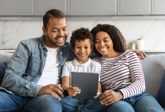 Black family with preteen son smiling joyfully while using digital tablet together