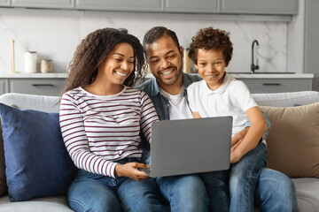 Cheerful black family having fun with laptop at home, watching photos together