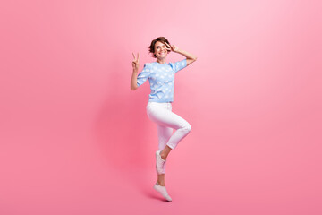 Full size portrait of pretty active girl jump demonstrate v-sign near eye have good mood isolated...