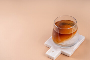 Cognac or whiskey with ice, strong alcohol cocktail with frozen glass on light beige background copy space