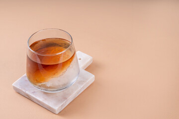 Cognac or whiskey with ice, strong alcohol cocktail with frozen glass on light beige background copy space