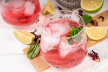 Hibiscus sour alcoholic cocktail or non-alcoholic mocktail, hibiscus mezcal margarita drink with ice, lime and mint on a light background