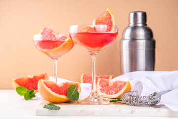 Grapefruit martini cocktail with cold champagne. Refreshing summer cocktail with garnish of a piece of grapefruit and mint on a light background with bar tools and ingredients