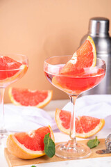 Grapefruit martini cocktail with cold champagne. Refreshing summer cocktail with garnish of a piece of grapefruit and mint on a light background with bar tools and ingredients