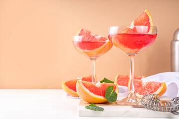 Grapefruit martini cocktail with cold champagne. Refreshing summer cocktail with garnish of a piece of grapefruit and mint on a light background with bar tools and ingredients