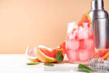 Grapefruit margarita or lemonade cocktail with cold champagne. Refreshing summer cocktail with garnish of a piece of grapefruit and mint on a light background with bar tools and ingredients