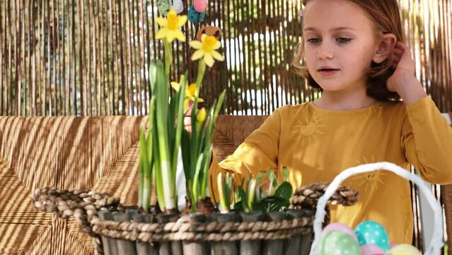 Happy child girl make spring Easter composition with yellow flowers, paper colored Easter bunny, eggs basket. Children prepare decoration present for Easter party at home. Kid creativity and hobby DIY