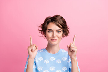 Portrait of positive nice girl indicate fingers up above empty space proposition isolated on pink...