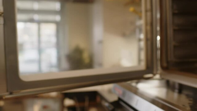 Close up view of professional baker in mitt opening oven and removing ready croissants on tray while working in commercial kitchen