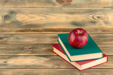 Red apple on hardback books, wooden background with space for text. - Powered by Adobe