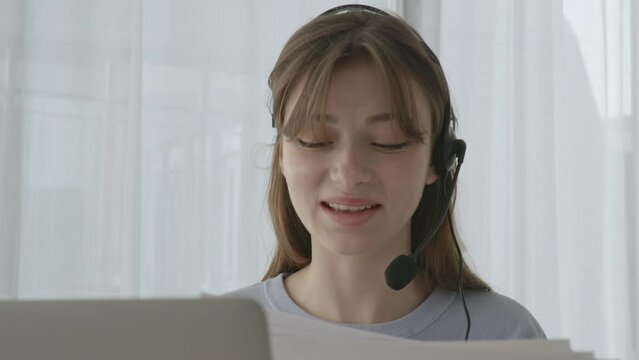 A young woman talking on her headset and looking between her computer and paperwork