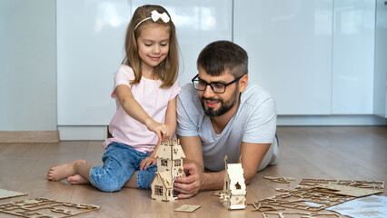 Father and child build wooden construction set sitting on floor at home. Happy family play with construction kit. Childrens designer. Leisure