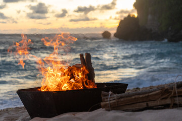 A bonfire crackles on the beach at twilight, with the flames dancing against the backdrop of a...