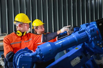 Male Caucasian engineers with safety helmets operating and discussing robotics in an industrial environment