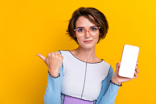 Portrait of attractive nice person direct finger showing empty space smart phone screen isolated on yellow color background