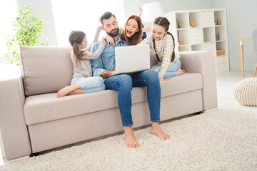 Full size photo of four people guy closed eyes sit on couch crazy funky girls use laptop hand pull dads ear indoors