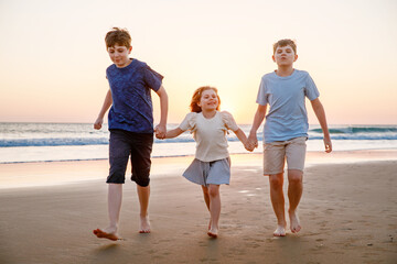 Portrait of three children, happy kids on beach at sunset. happy family, two school boys and one little preschool girl. Siblings having fun together. Bonding and family vacation