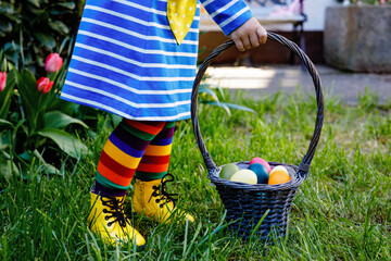 Close-up of of toddler girl with colorful stockings and shoes and basket with colored eggs. Child...