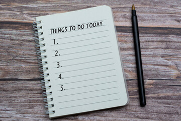 Notebook with things to do today list on wooden desk with pen.