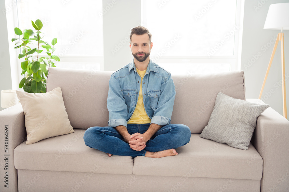 Wall mural full length body size young guy in jeans outfit sitting on couch relaxing at home on weekends