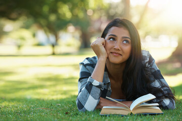 Happy woman, student and thinking with book for reading, literature or studying on green grass....