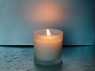 Scented candle on silver surface with water drops, peace and meditation concept.