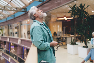 Contemplative senior Caucasian male professional holding glasses and smartphone in an office...