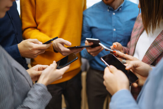 Group of young people using mobile phone. Happy colegios sitting side by side in a modern office using digital devices. Modern lifestyle with information technology gadget, education, social network.