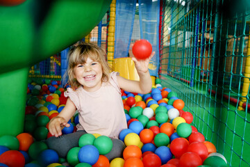 Active little girl playing in indoor playground. Happy joyful preschool child climbing, running, jumping and having fun with colorful plastic balls. Indoors activity for children.