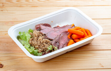Veal sous vide with juicy carrots. Healthy diet. Takeaway food. Eco packaging. On a wooden background.