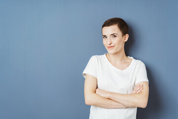 Confident Young Woman With Short Hair Posing Against Blue Wall, Arms Crossed, Smirking at Camera,...