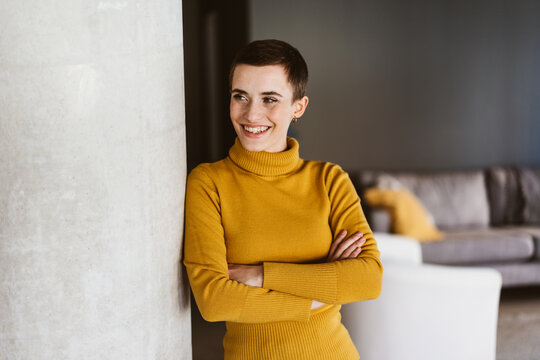 Young Woman with Short Hair, Clad in a Yellow Turtleneck, Leaning against a Pillar in a Joyful Living Room Moment