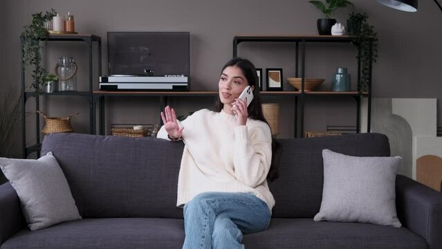 Cheerful Caucasian woman talking during phone call on the sofa. Relaxation and resting, home leisure activity, contacting with friends, remote communication.