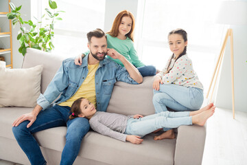 Portrait of four persons cheerful man sit o f sofa with adorable positive girls enjoy free time weekend home indoors