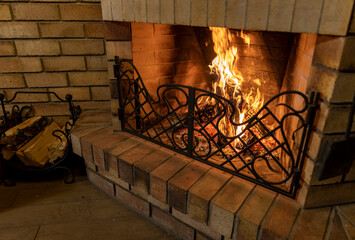old brick fireplace with a forged grate and burning wood
