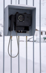 An old black telephone for communication with a checkpoint hangs on a metal fence
