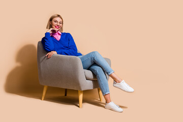 Obraz na płótnie Canvas Photo of cheerful young blonde hair psychotherapist sitting gray armchair relaxed waiting for patient isolated on beige color background