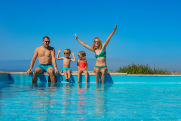 Fototapeta na wymiar Parents with kids take pleasure to sit on the edge of pool