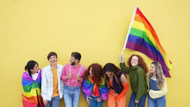 Diverse group of young people celebrating gay pride festival day - Lgbt community concept with guys and girls hugging together outdoors - Multiracial cheerful friends standing on a yellow background