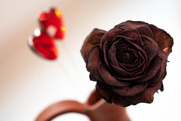 a dried rose in a ceramic jug and two red glass hearts in close-up