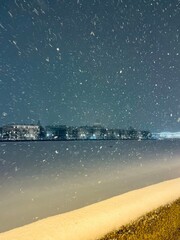 snowfall at the city river, frozen city, night time, dark sky and white snow