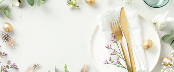 table setting with white plate, golden cutlery, easter eggs and spring branches