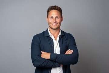 Portrait of a handsome young man standing with arms crossed against grey background