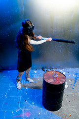 A girl in a protective mask smashes a glass with a baseball bat in the destruction room to relieve stress