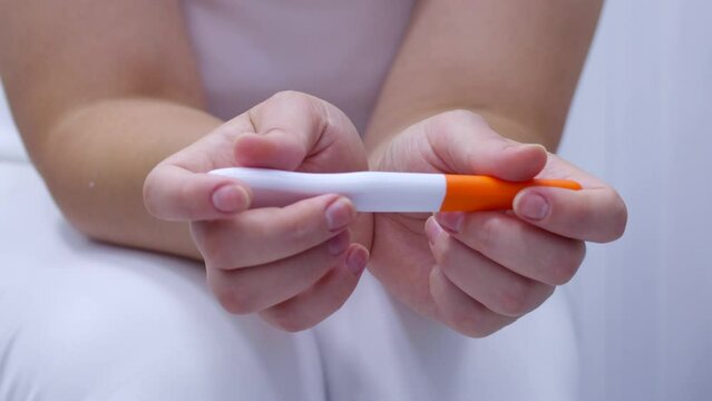 Woman hands holding pregnancy test waiting for positive result in bathroom. Girl checking plastic test kits at home. Fertility and healthcare concept