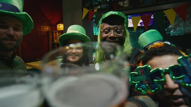 POV UGC footage of clanging glasses of beer with multiracial friends via online video call and celebrating Irish Saint Patricks Day indoors